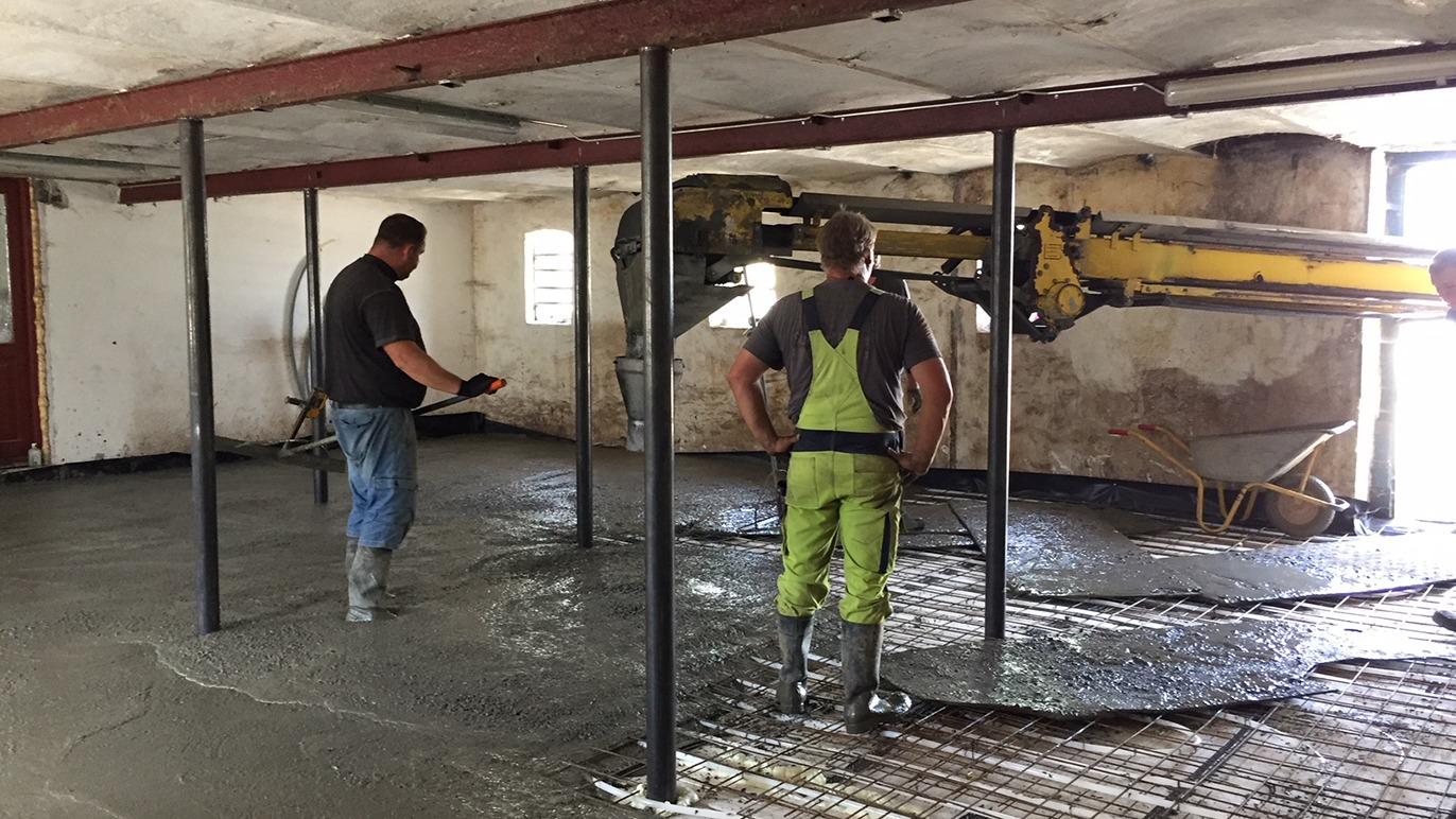 To mænd arbejder med at hælde beton i en bygning, mens en betonpumpe er i brug.