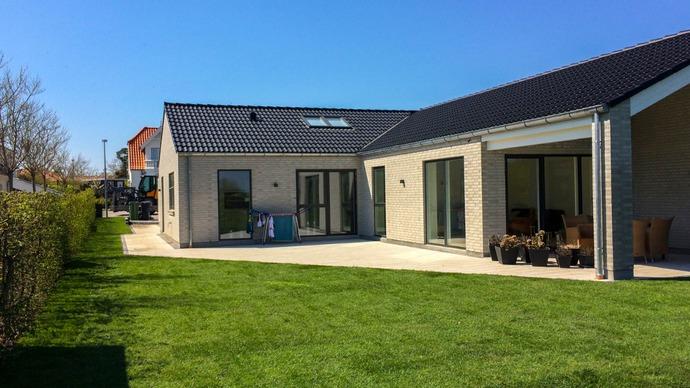Moderne hus med græsplæne og terrasse, beliggende i et roligt boligområde under en klar blå himmel.