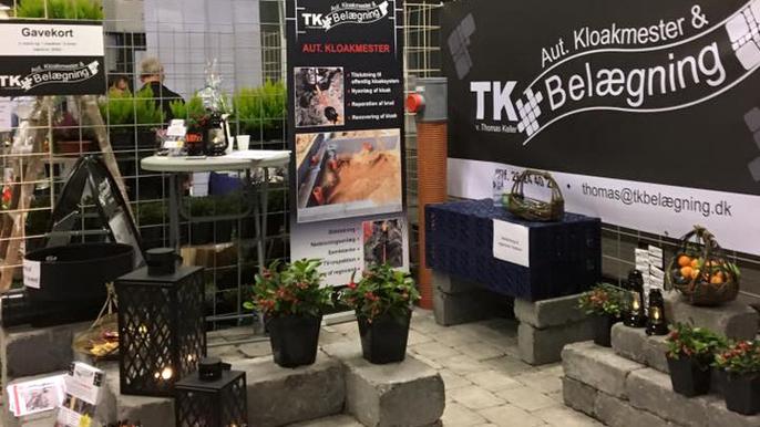Stands med planter, belysning og information om belægningsarbejde på en messe.
