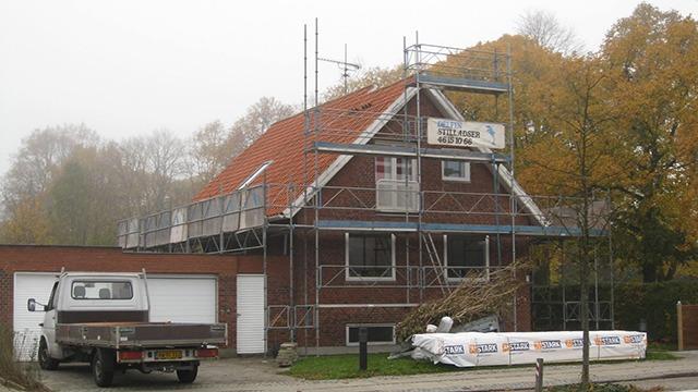 Et hus under konstruktion med stillads, rød tag og en lastbil parkeret foran.