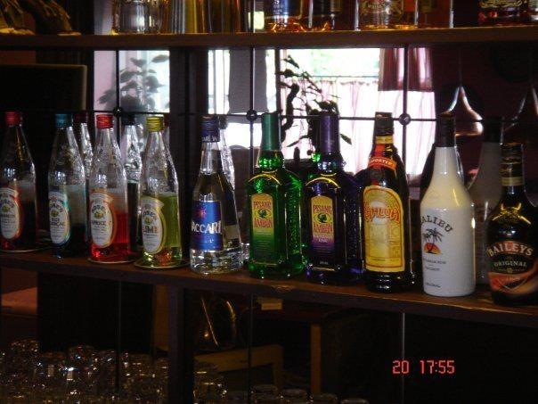 En hylde med forskellige flasker spiritus og sodavand i en bar, herunder farverige likører og mineralvand.