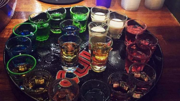 En rund bakke med farverige shots i forskellige glas, herunder grønne, røde og klare shots.