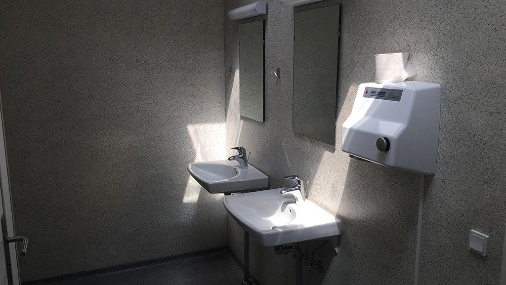 Et lyst badeværelse med to håndvaske, spejle og en håndtørrer på væggen.
