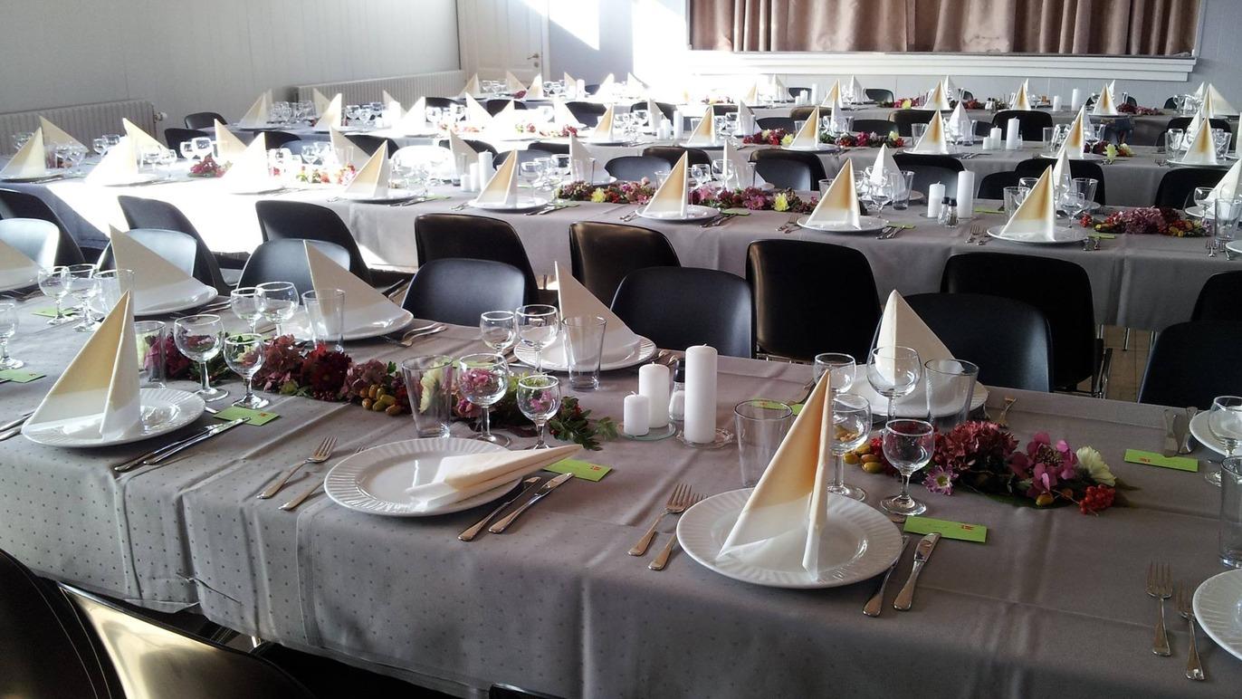 Et festligt dækket bord med servietter, glas og tallerkener i en elegant sal.