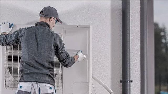 En tekniker rengør en klimaanlægsenhed på en væg i et moderne hjem.