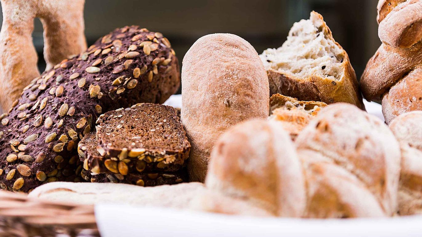 En kurv med forskellige typer brød, herunder frøbrød, rundstykker og groft brød.