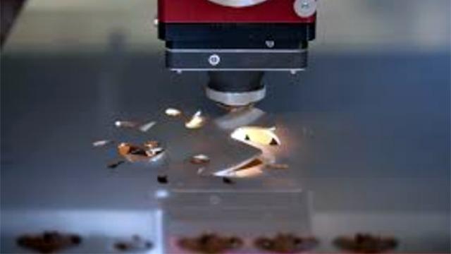 Laserudskærer i aktion, der skærer præcise former i metalplade med lys og røg.