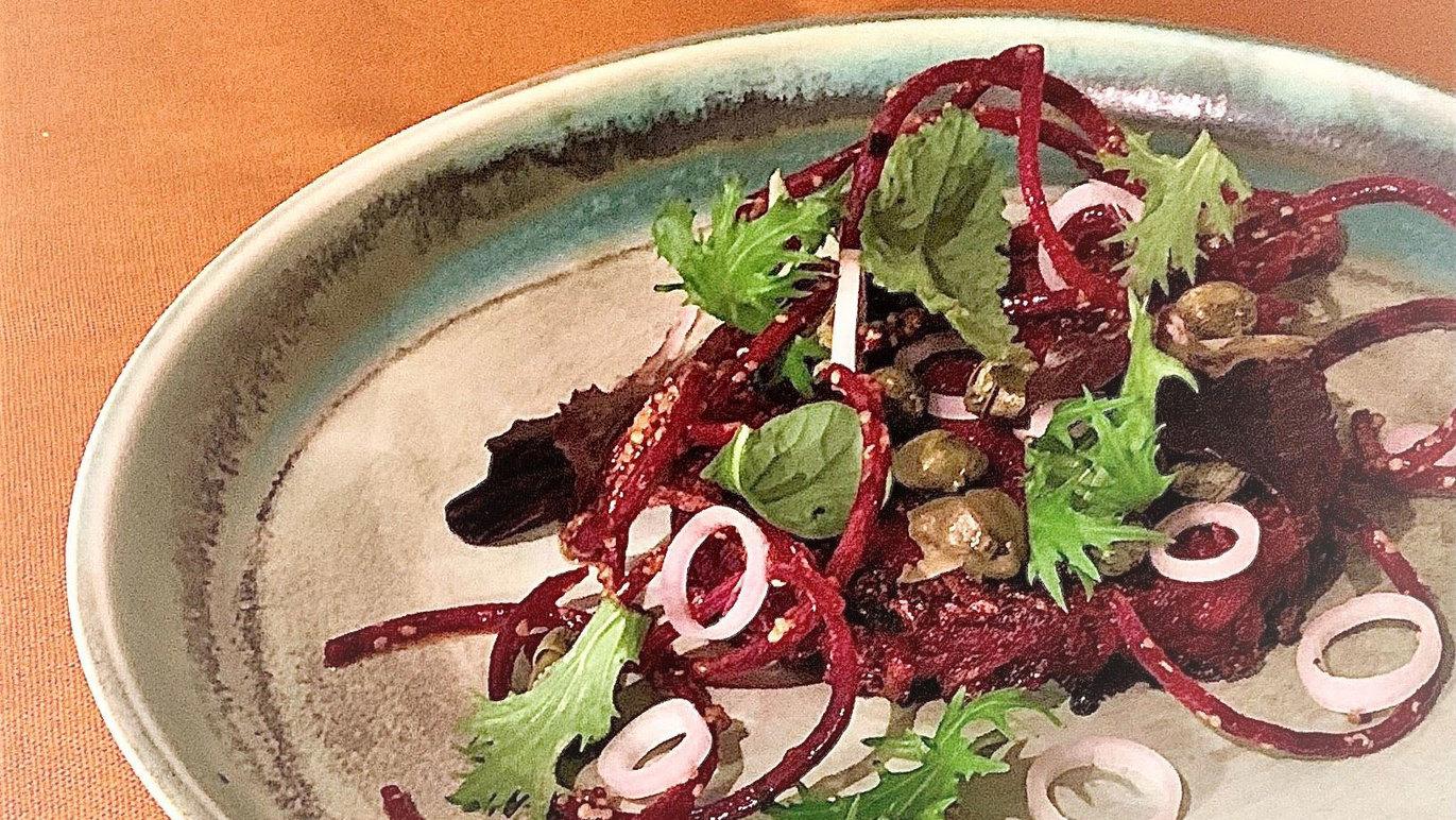 En tallerken med rødbedesalat, toppet med friske urter, løg og græskarkerner.