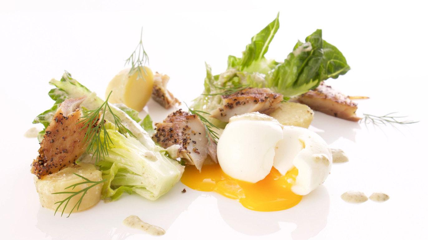 En elegant anretning med sprød salat, grillet fisk, kartofler og en blød æggeblomme.