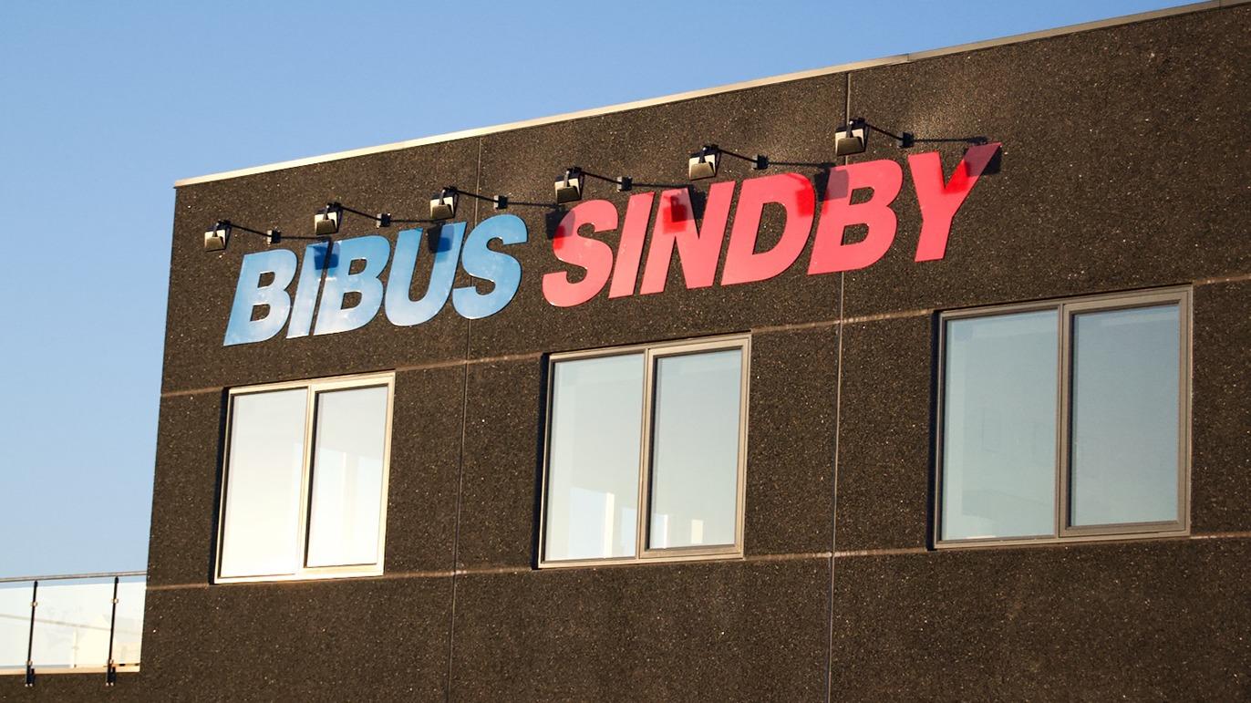 Bibus Sindby skilt på bygning med vinduer og klar blå himmel i baggrunden.