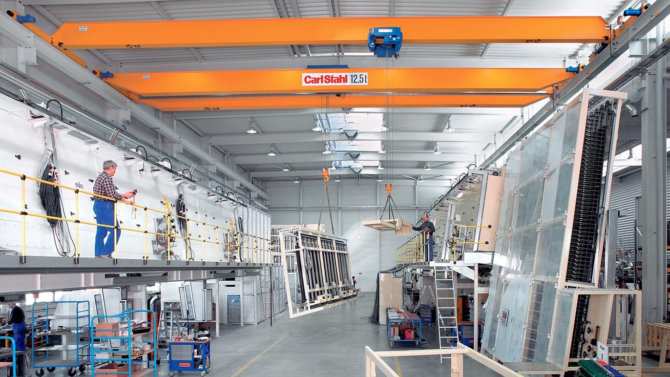 Industrielt værksted med kran, medarbejdere, og store glasruder i produktion.