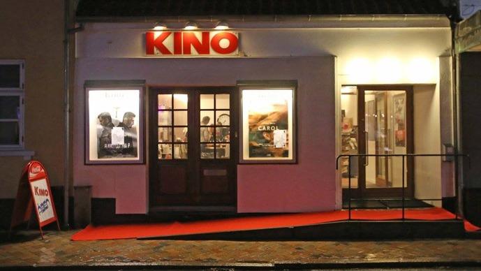 Kino biograf med rød løber og vinduer, der viser filmplakater, beliggende i en by.