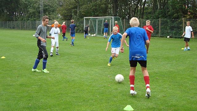 Børn spiller fodbold på en grøn bane, mens de træner og øver deres færdigheder.