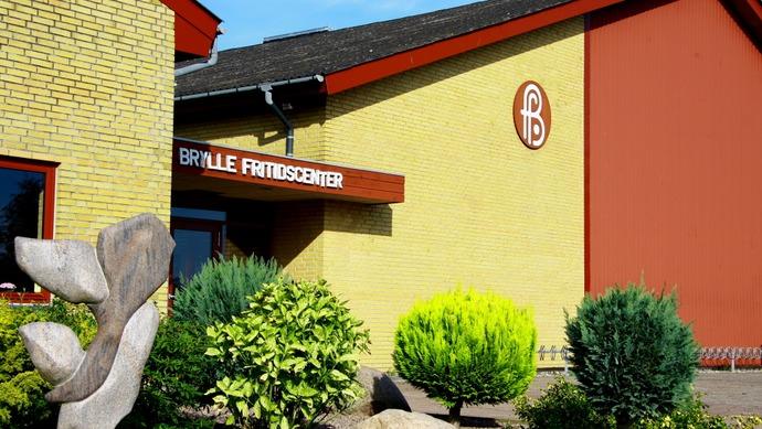 Bygningen af Brille Friskole med gule og røde vægge, omgivet af grønne buske og træer.