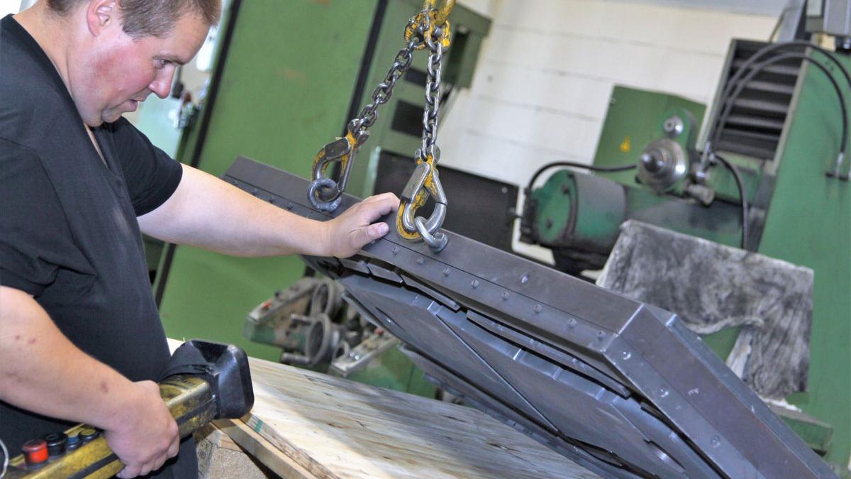 En mand arbejder med en stor metalplade, der hæves af en kran i en fabrik.