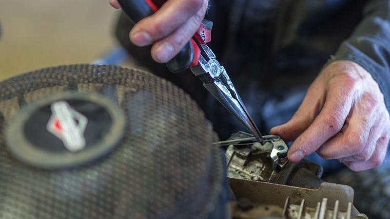 En person arbejder med en motor ved hjælp af tang til at justere dele.