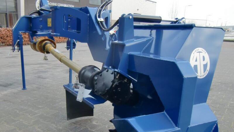 Blå maskine til landbrug med en kraftudtag og hydraulisk arm, placeret på en gårdsplads.