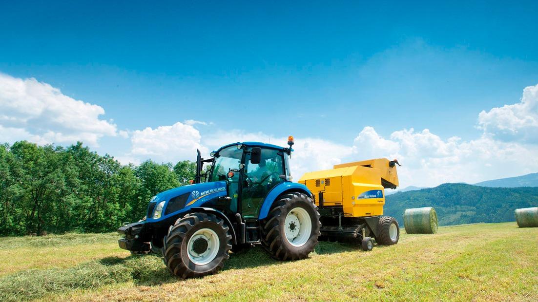 En blå traktor arbejder på en mark med en gul høstmaskine under en klar blå himmel.