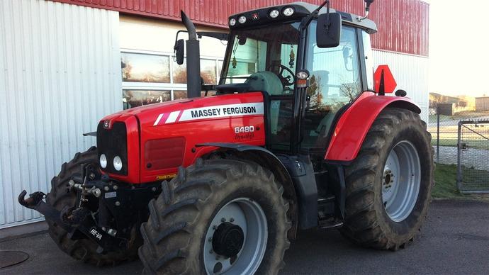 Rød traktor fra Massey Ferguson parkeret foran en bygning med store dæk og moderne design.