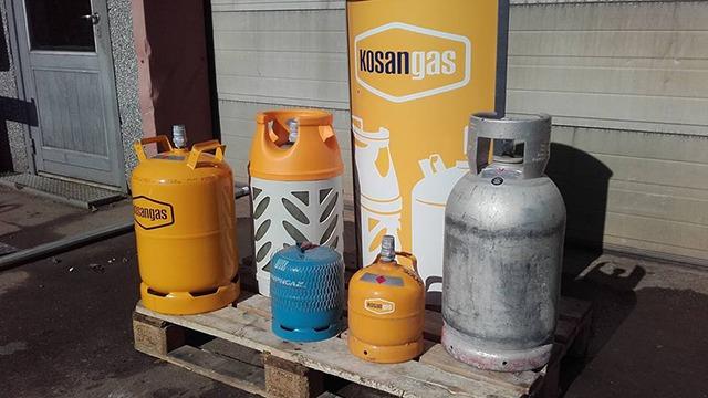 Billede af gasflasker i forskellige størrelser og farver, herunder orange og grå, præsenteret på en palle.