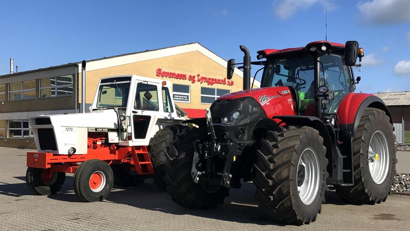 To store traktorer parkeret foran en bygning, en rød traktor og en hvid traktor med orange detaljer.