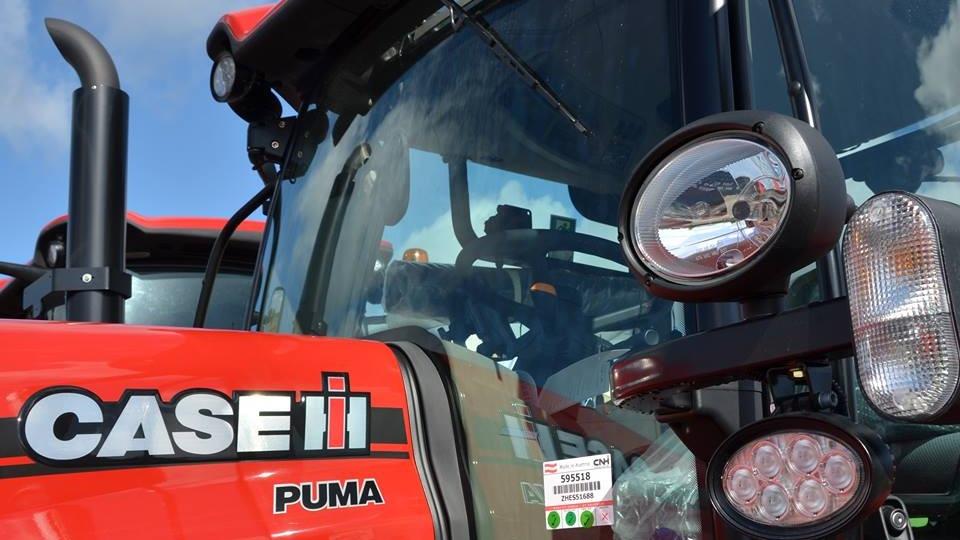 Rød CASE IH Puma traktor med detaljeret front og spejl, klar til brug på en gård.