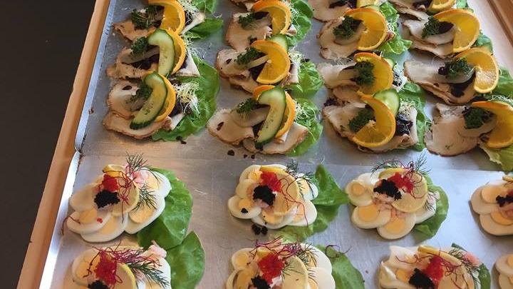 Lækre smørrebrød med fisk, grøntsager og pynt på salatblade, præsenteret på en bageplade.