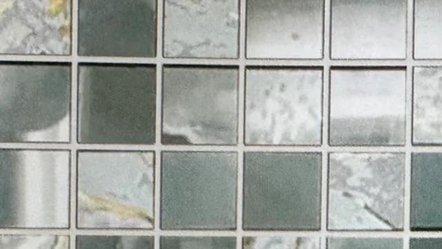Et nærbillede af en mosaikflisevæg med grå og sølvfarvede firkanter.
