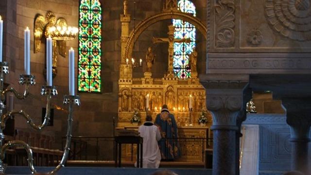 En person står foran et smukt alter i en kirke med farverige vinduer og stearinlys.