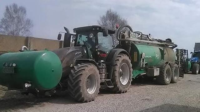 En stor traktor med en gyllevogn parkeret på en grusvej i en landbrugsområde.