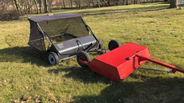 En græsslåmaskine med en rød opsamler på en græsplæne i et solrigt område.