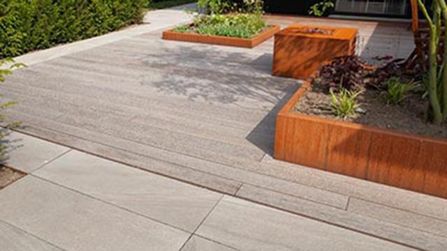 Moderne terrasse med grå fliser og træbede fyldt med planter.