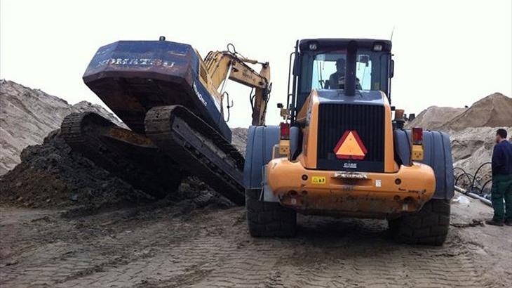 En gravemaskine arbejder på en byggeplads med sand og jord i baggrunden.