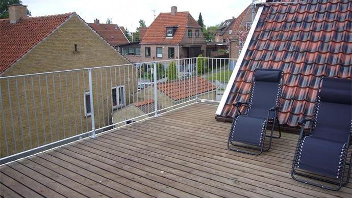 Tagterrasse med trædæk, to liggestole og udsigt over nabohuse med røde tage.