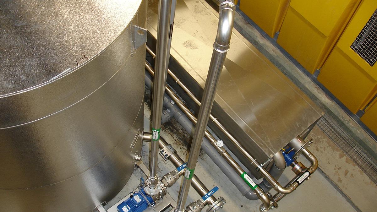 Billede af en metalbeholder med rør og ventiler i et industrielt miljø.