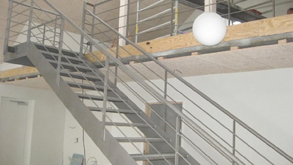Ståltrappe med gelænder i moderne indretning, der fører til en balkon med en stor lampe.