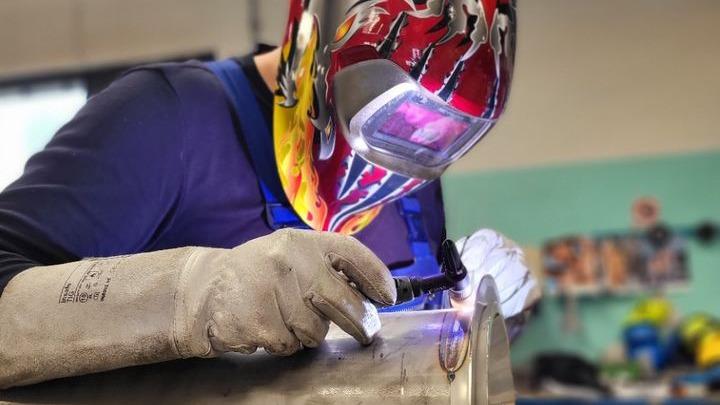 En svejser arbejder koncentreret med en svejseapparat på metal, iført beskyttelsesbriller og handsker.
