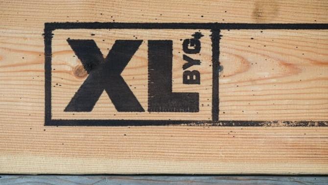 XL BYG logo trykt på en træplade, der viser brandets identitet og fokus på byggeri.