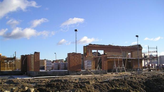 Byggeplads med mursten og stilladser under konstruktion af et hus. Blå himmel med skyer i baggrunden.