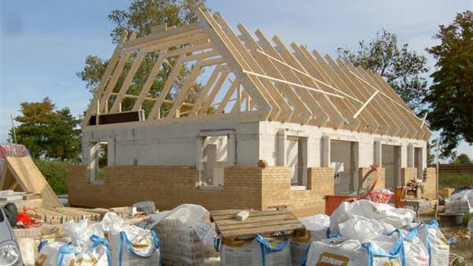 Byggeri af et hus med træramme, omgivet af byggematerialer og affald. Træstrukturen er synlig på taget.