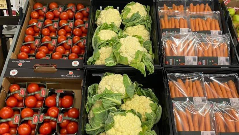 Friske tomater, blomkål og gulerødder præsenteret i kasser i en supermarked.