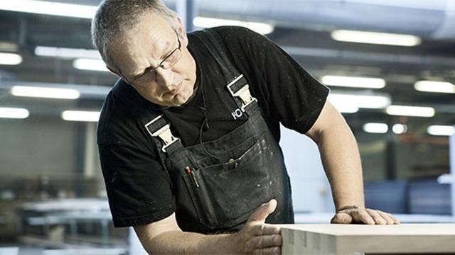 En håndværker arbejder koncentreret med træ i et moderne værksted.