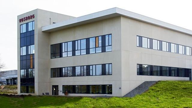 Moderne kontorbygning med store vinduer og grøn græsplæne foran.