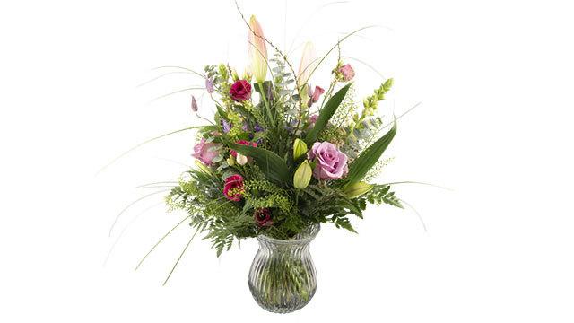 En farverig buket blomster i en glasvase med roser, tulipaner og grønne blade.