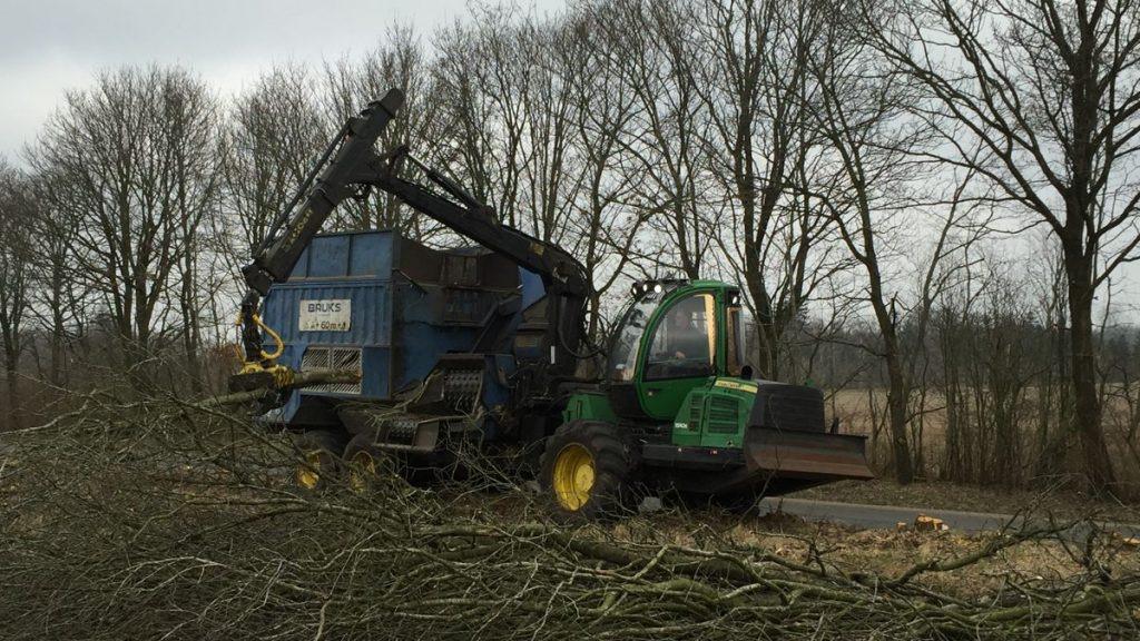 En stor træfældningsmaskine arbejder på en skovvej med grene og træer omkring.