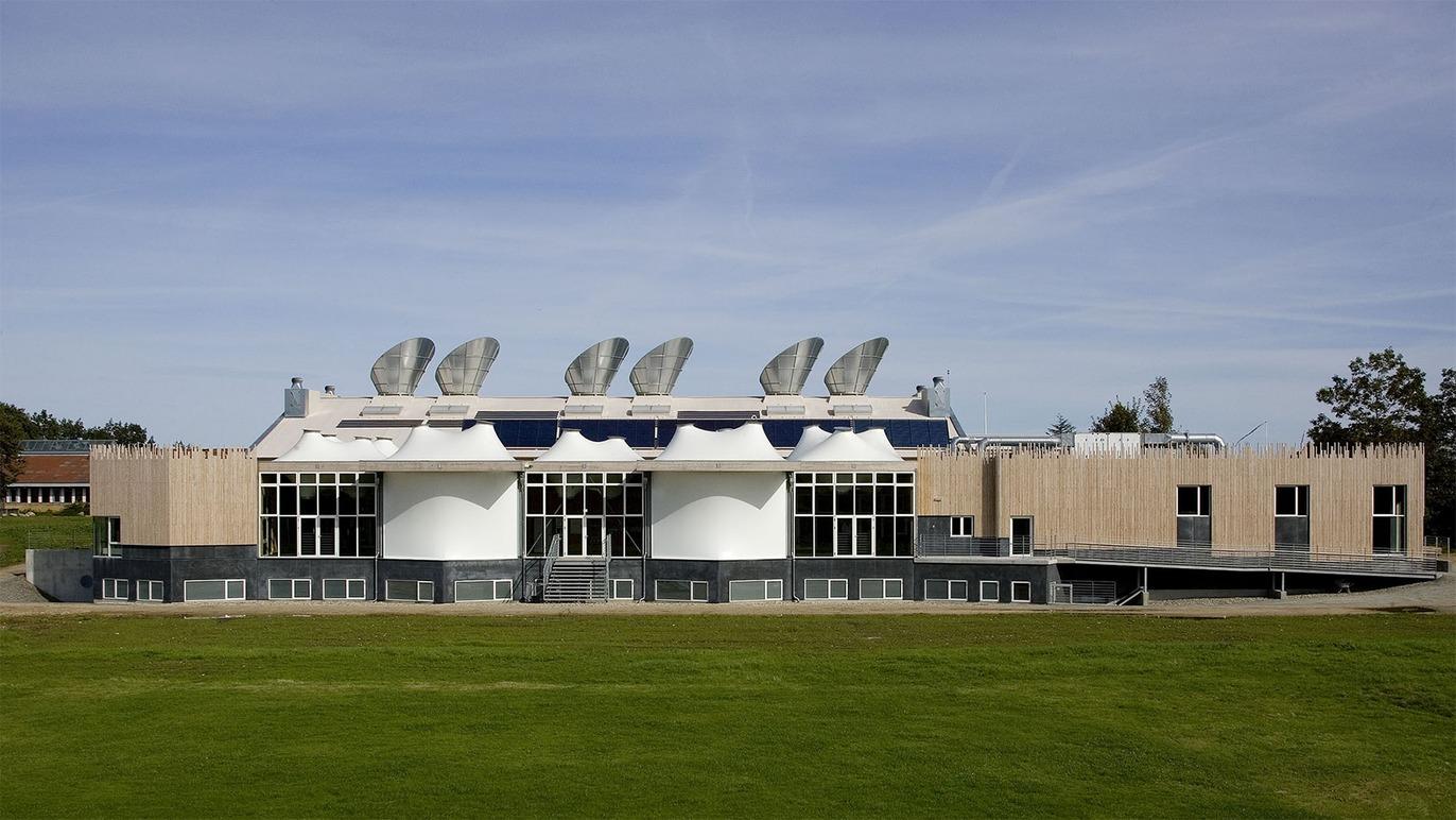 Moderne bygning med solpaneler og store vinduer, beliggende på en grøn græsplæne under en blå himmel.