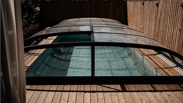 Et indendørs swimmingpool med glasoverdækning og træterrasse omkring.