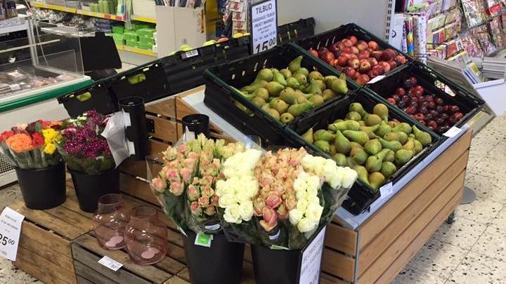 Blomster og frugt i en butik, med buketter af roser og forskellige frugter som pærer og æbler i kasser.