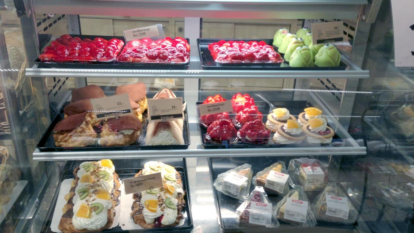 Bageriudstilling med forskellige kager, tærter og dessertanretninger i en køledisk.