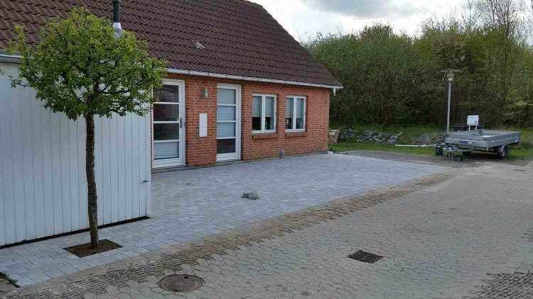 En rød murstenshus med en lille træ i forgrunden og en grusvej ved siden af.
